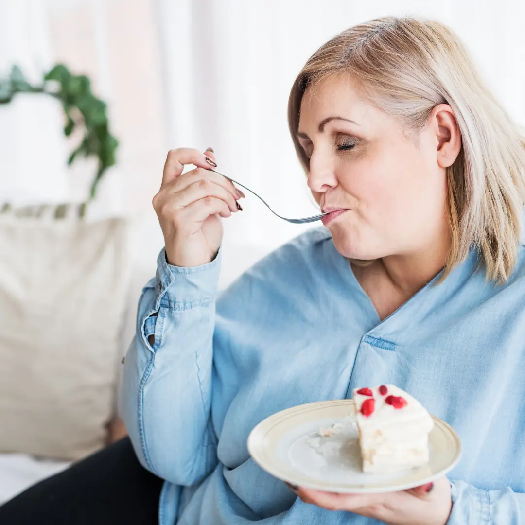 Mujer de mediana edad con sobrepeso comiendo una tarta saboreándola mucho como si buscara consuelo en la comida.