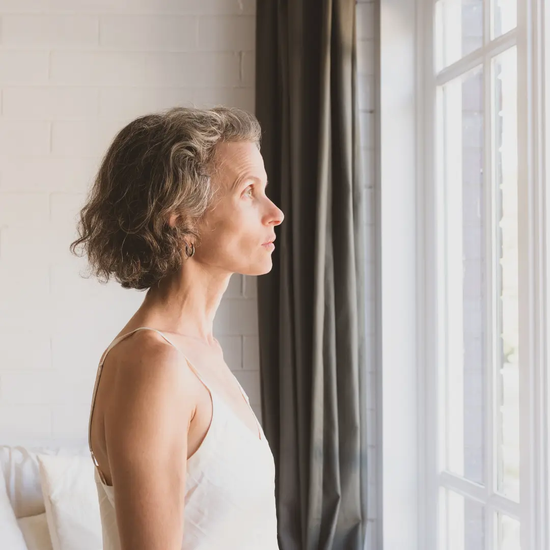 Mujer de mediana edad mirando detrás de la ventana con la mirada ausente y perdida